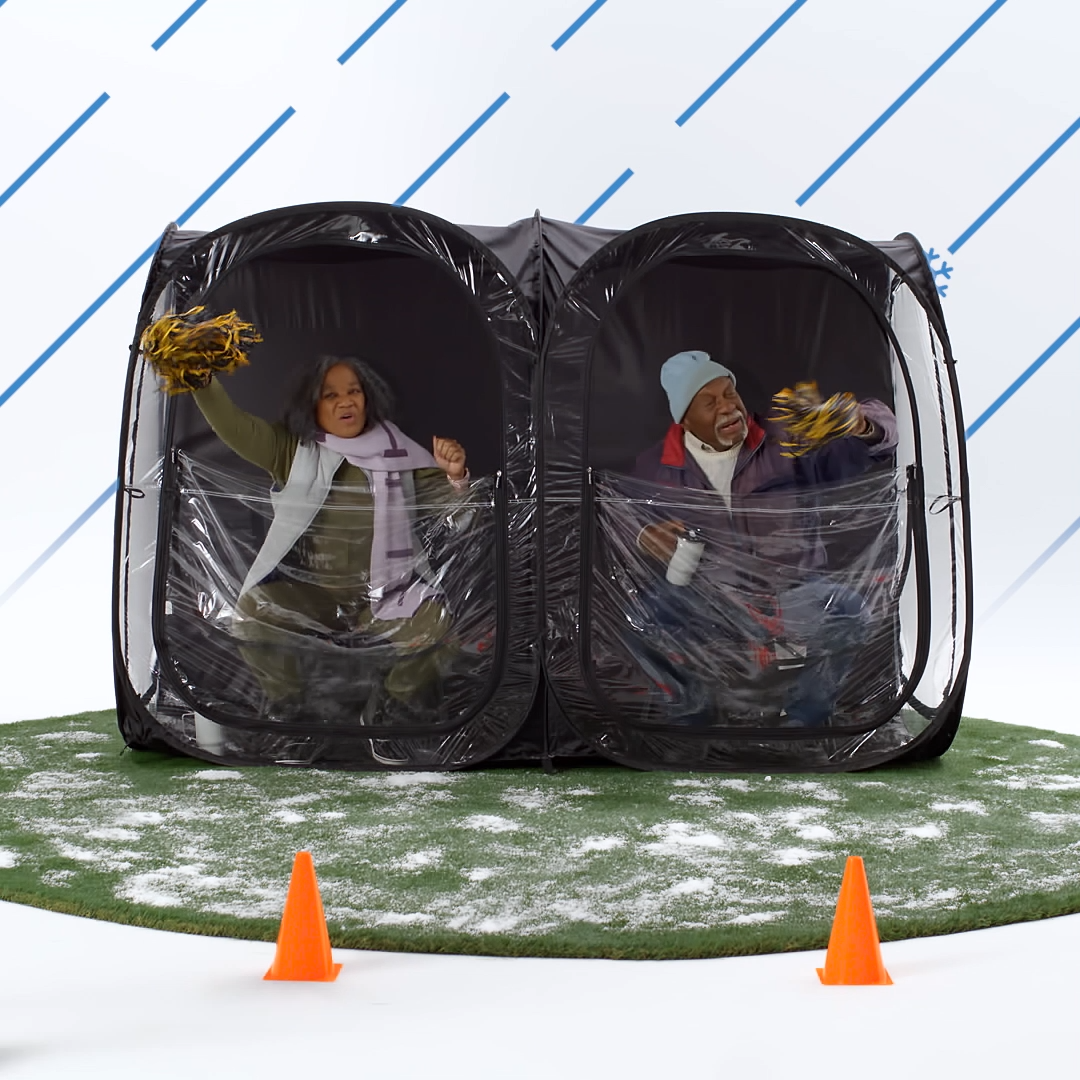 Two grandparents sit inside a black Weatherpod and cheer on a game