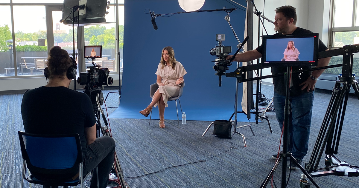 Behind the scenes image of a woman being interviewed on a blue backdrop. 