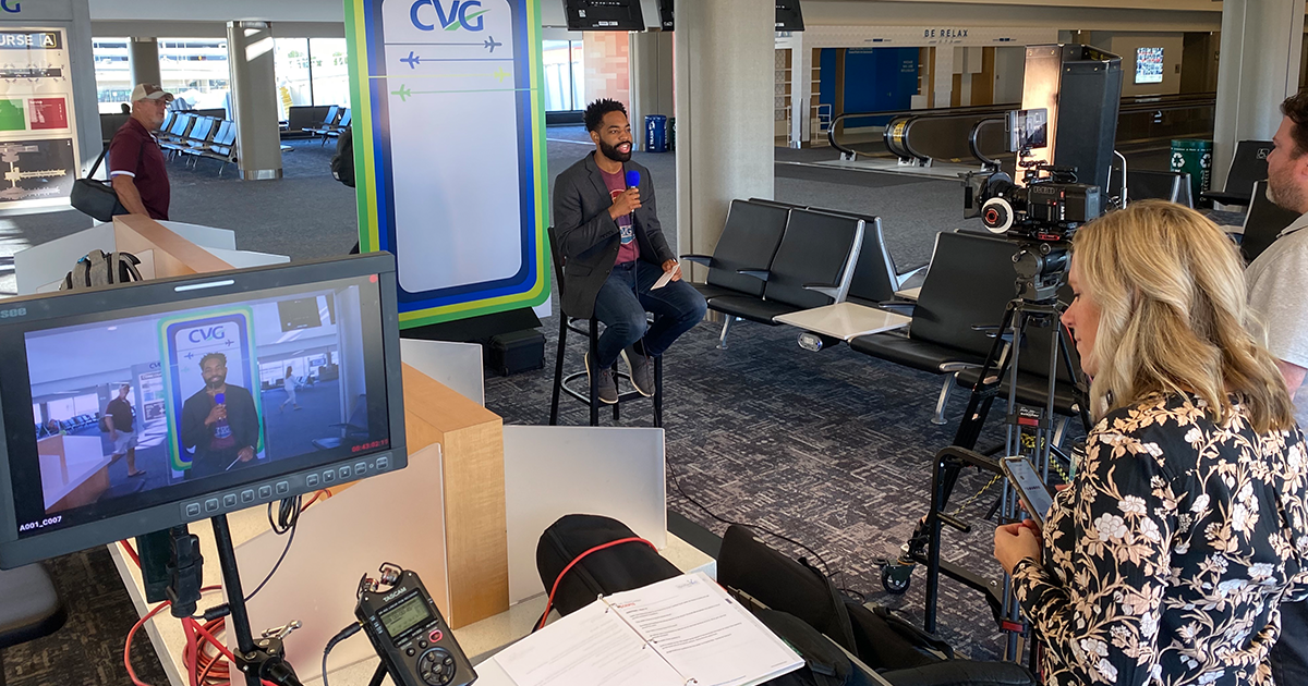 Behind the Scenes image of a video shoot for CVG Triva Tuesday with the host in front of a backdrop.