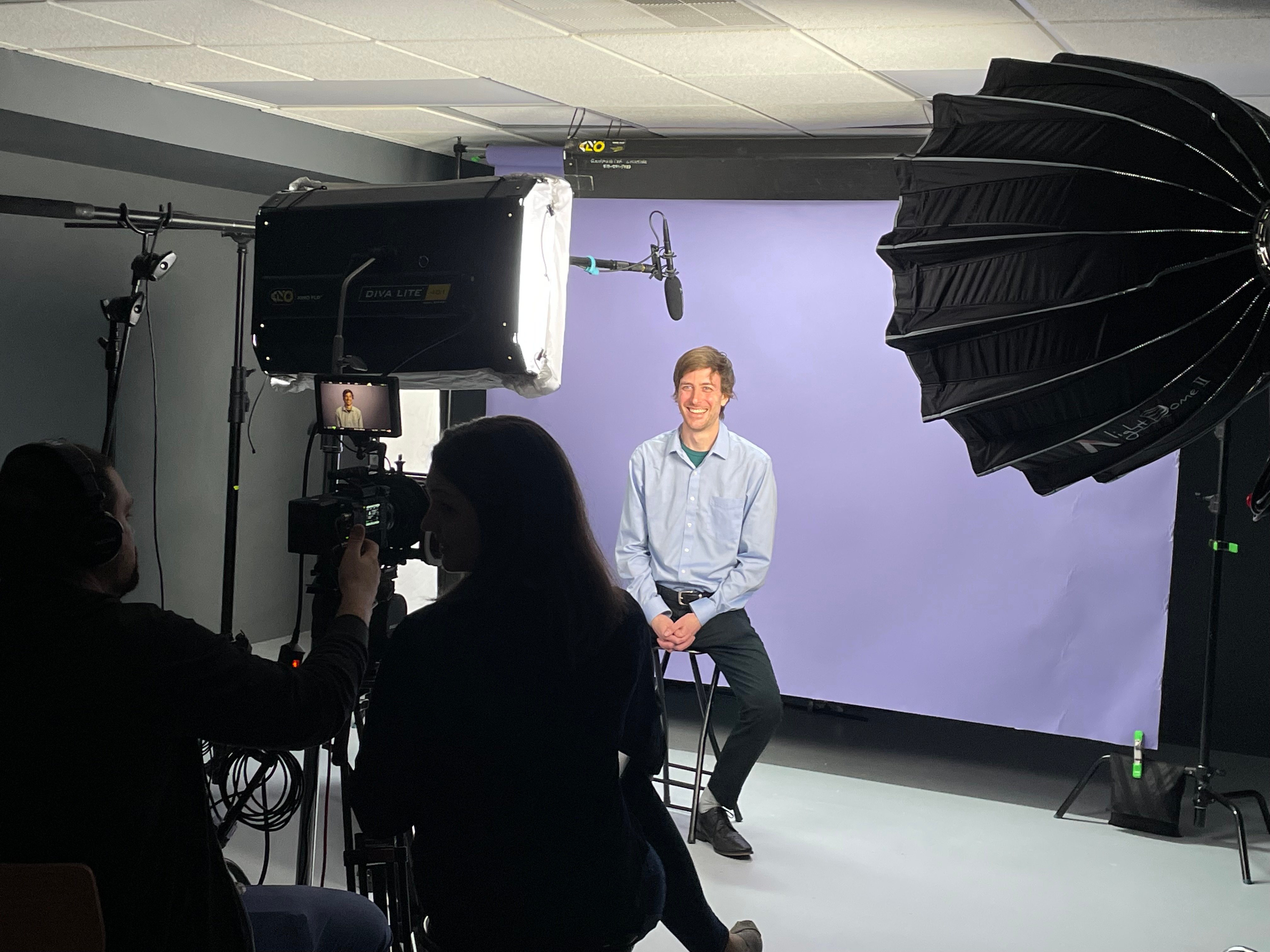 Erik Larsson sits in a video studio in front of a purple backdrop being interviewed. 