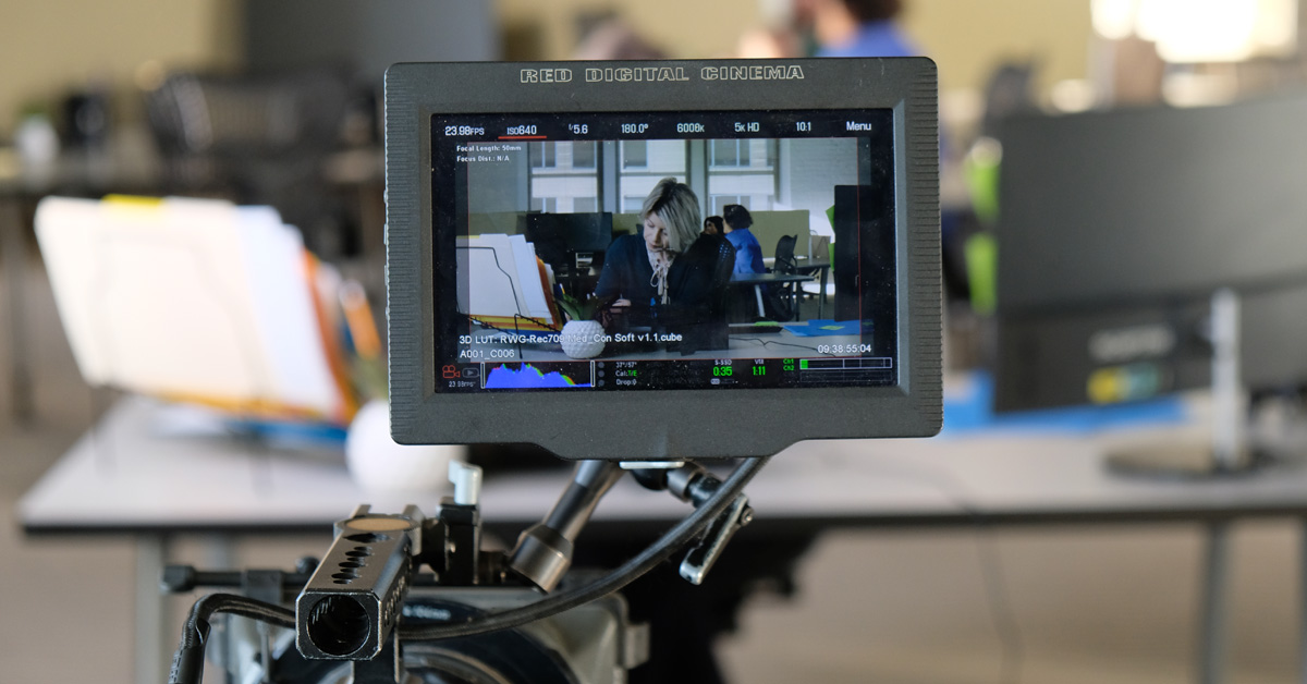 Camera monitor shows a shot of a woman working at a desk